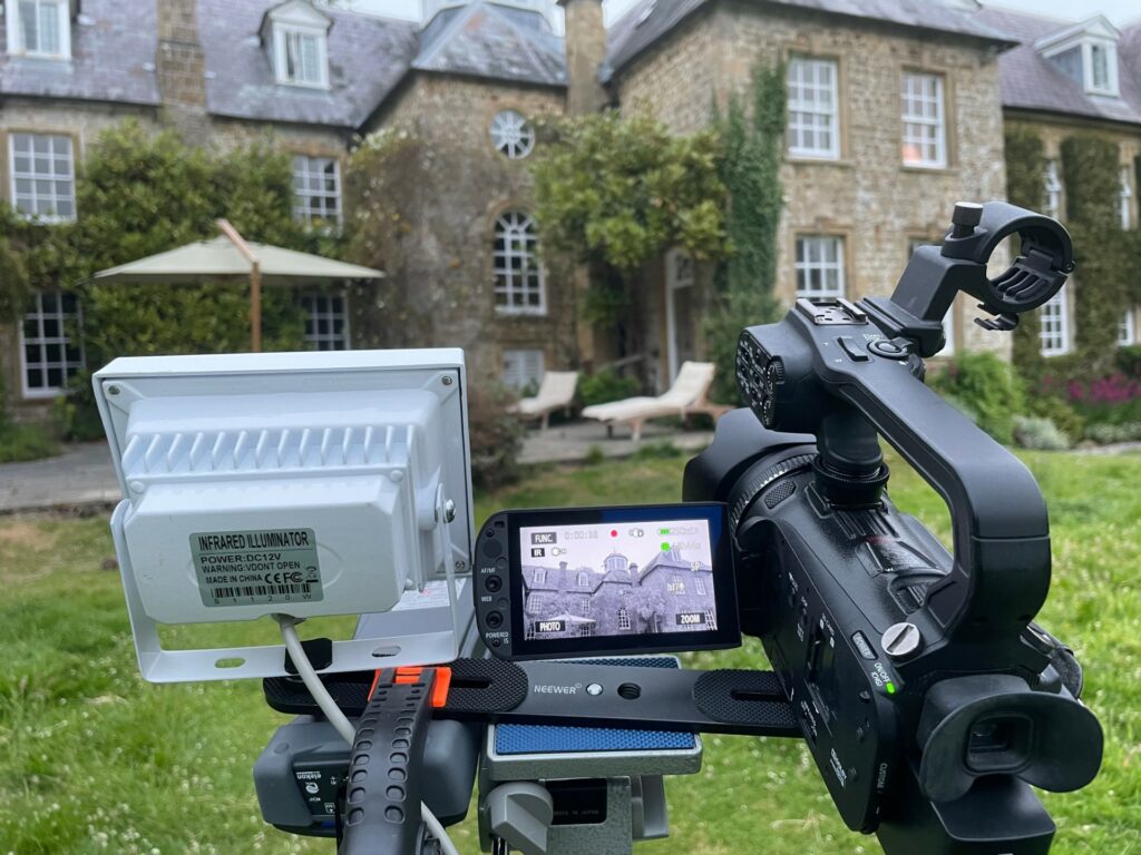 Infrared camera setup in foreground pointed at a house in the background for bat survey