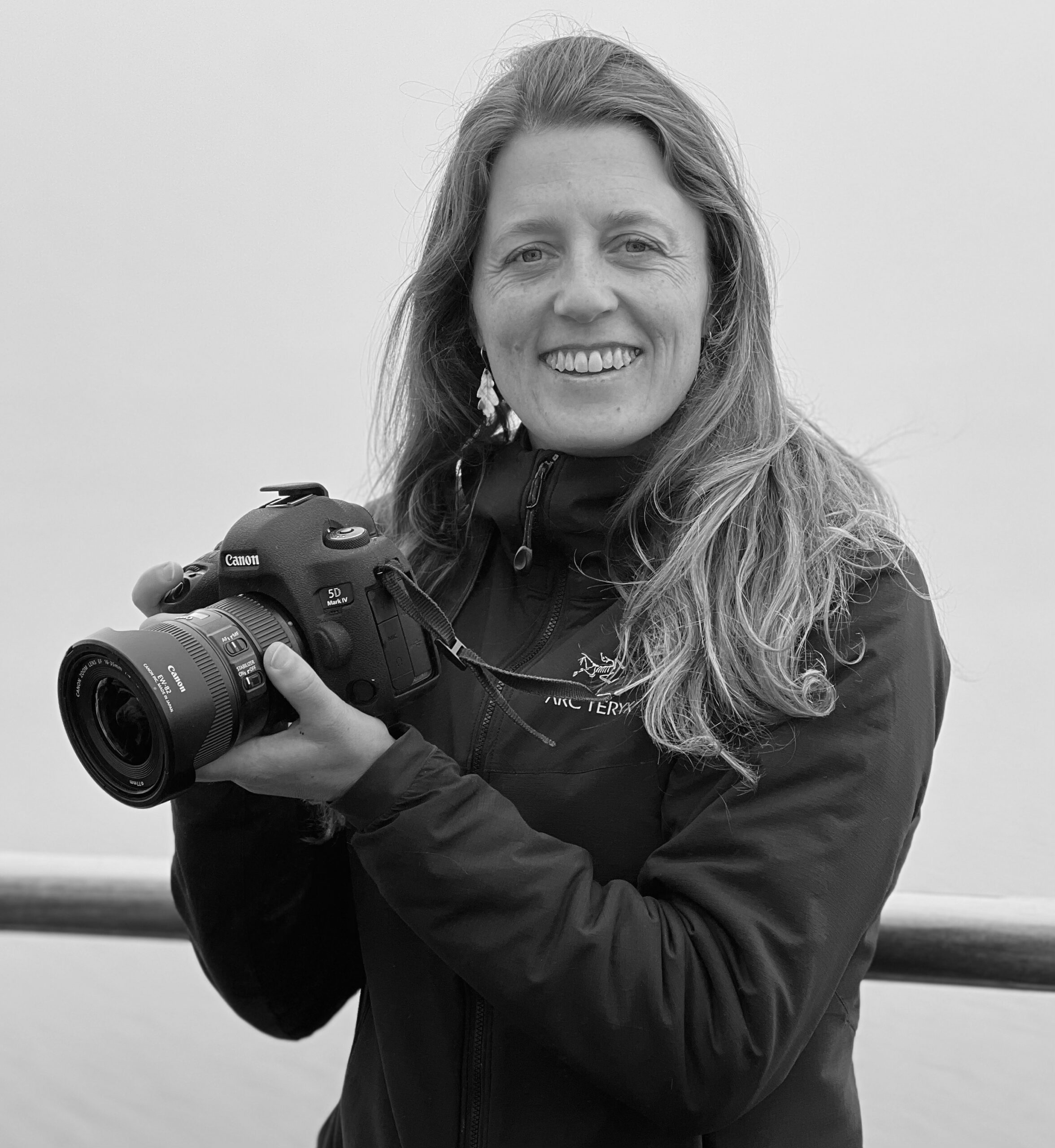 Black and white photograph of Michelle Sole, author of Antarctica: A Bird's-Eye View, holding a Canon camera and facing the camera.