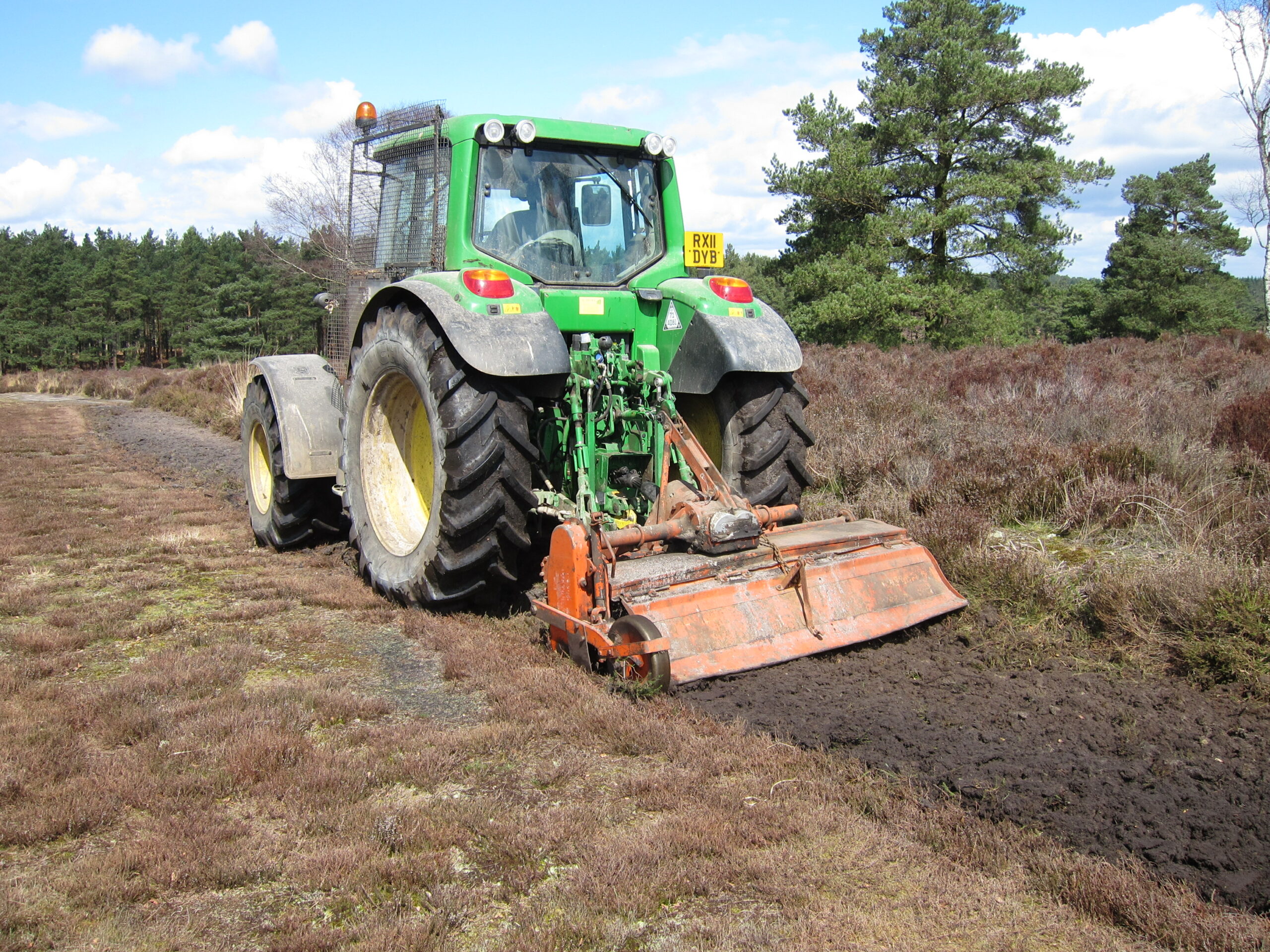 A green tractor ploughing a field as part of a reserve management programme.