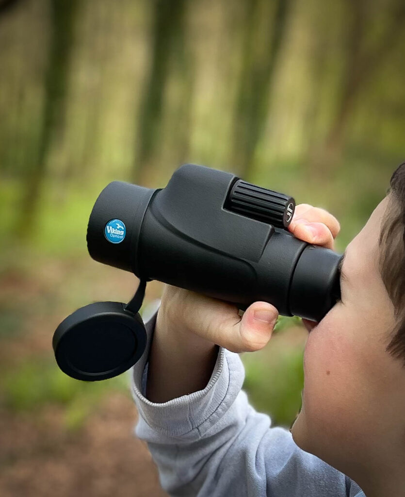 Young boy looking through a monocular in the woods. 