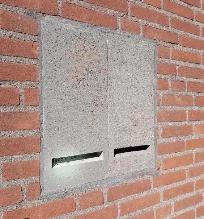 A large grey concrete box built into the wall with a thin slit at the bottom edge