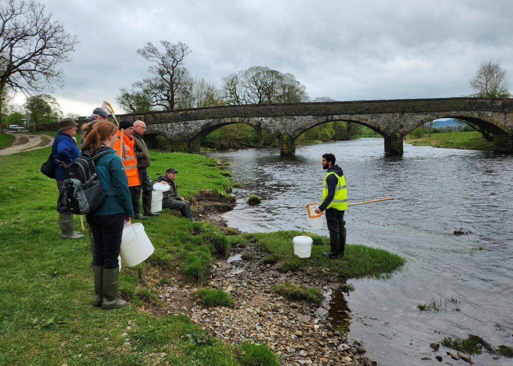 A group of volunteers standing around the riverside edge during a training day